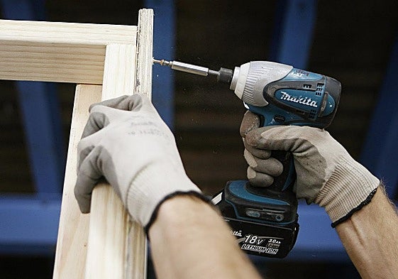 Un hombre utiliza un taladro atornillador para montar un mueble de madera.