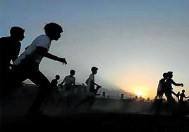 Un grupo de niños juega a fútbol durante un atardecer.