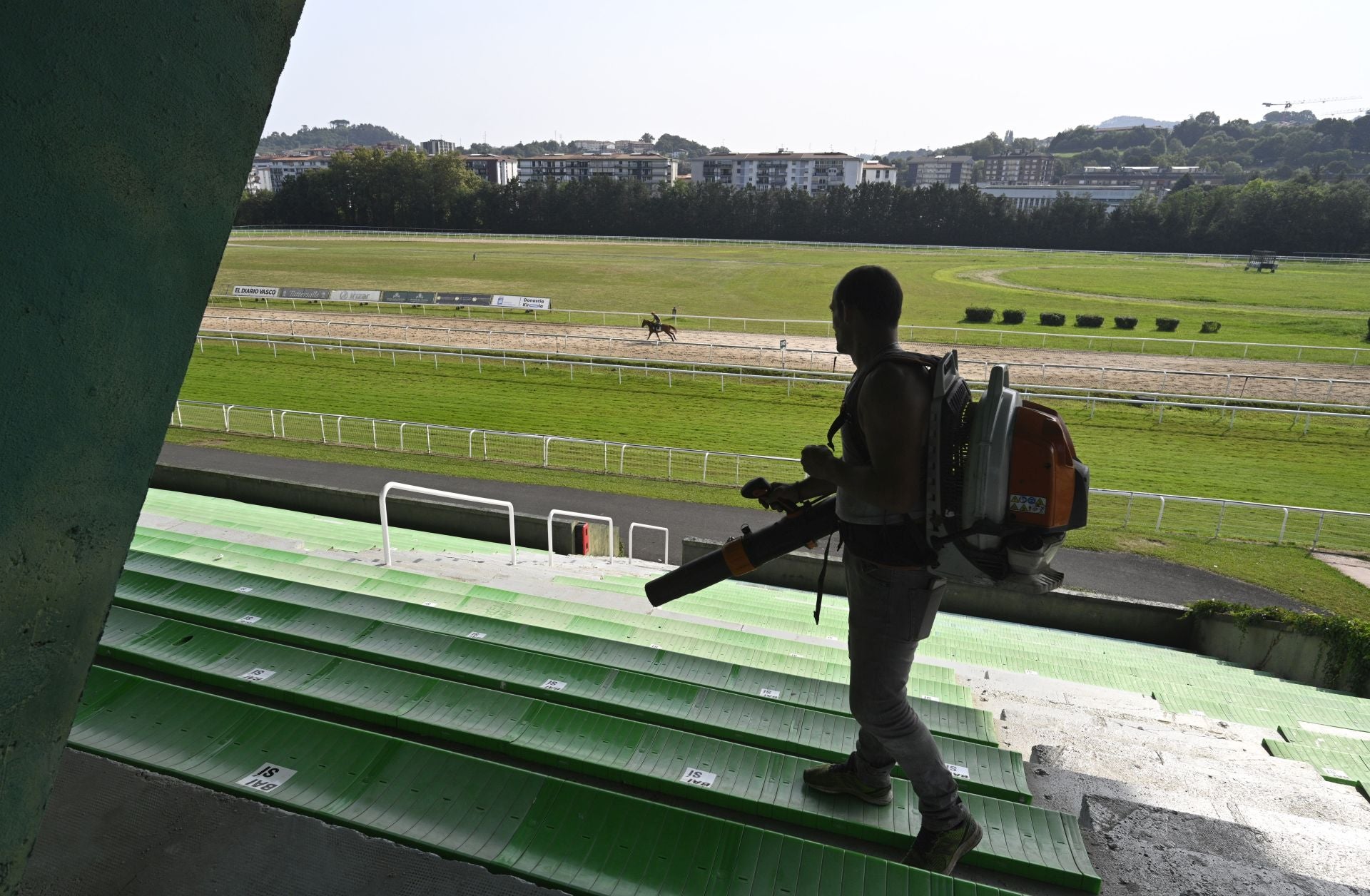 Un trabajador limpia con el soplahojas para dejar lista la grada del hipódromo