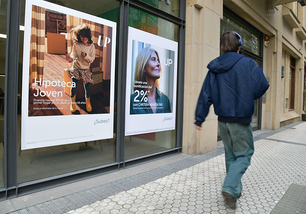 Un joven camina por delante de un escaparate con ofertas hipotecarias.