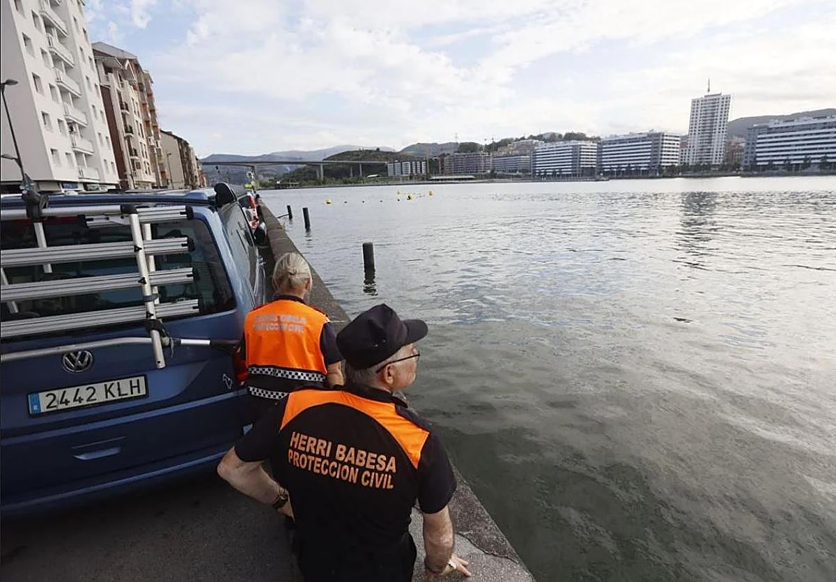 Dos integrantes de Protección Civil vigilan la Ría a la altura de Erandio, con Rontegi al fondo.
