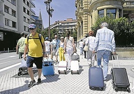 Turistas vienen y van con sus maletas por una céntrica calle de San Sebastián.