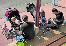 Dos padres dan de merendar a sus hijos en una zona de juegos.