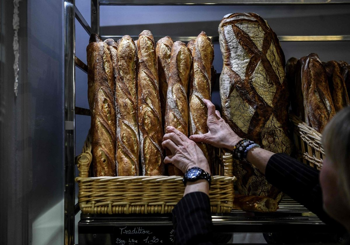 Una panadera sostiene diferentes barras en su comercio de París.