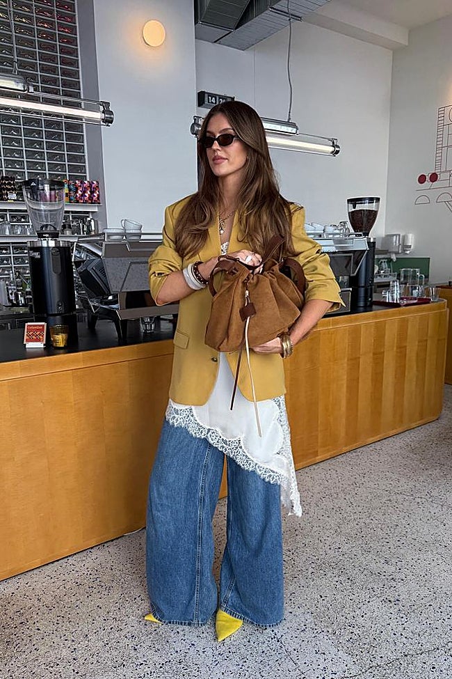 Creadora de contenido con un vestido lencero blanco superpuesto sobre los vaqueros, americana mostaza y salones amarillos.