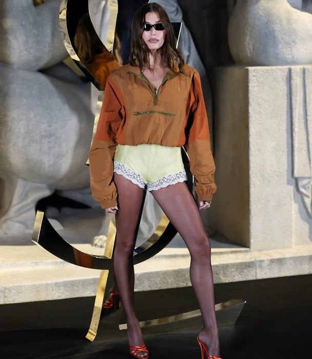 Hailey Bieber con una bomber deportiva naranja y pantalones de encaje en amarillo de Saint Laurent.
