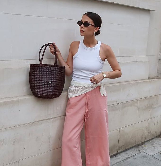 Camiseta de tirantes blanca con pantalón de lino rosa y pañuelo atado en la cintura con bolso de rafia.