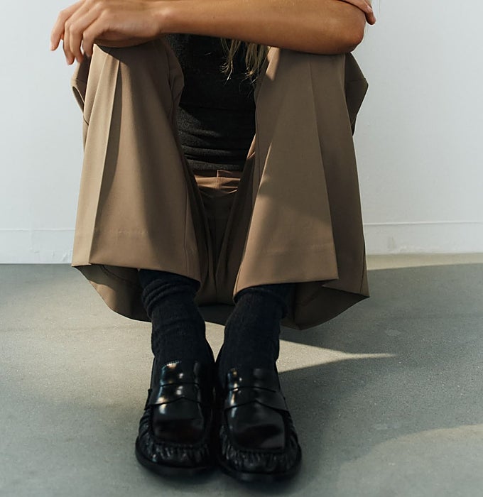 Pantalón de pinzas beige, mocasines fruncidos negros con calcetines.