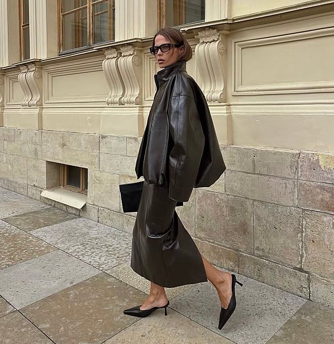 Chaqueta 'oversized' y falda midi de cuero en marrón chocolate, con mules negros de punta afilada y tacón bajo.