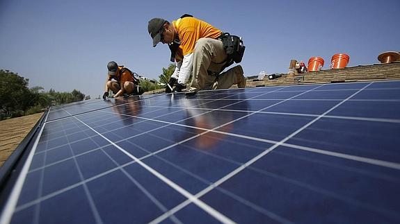 Operarios instalan paneles solares en el techo de una vivienda.