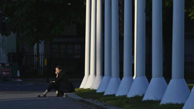 Una mujer descansa en una acera junto a las Casas del Parlamento durante el amanecer en Londres.