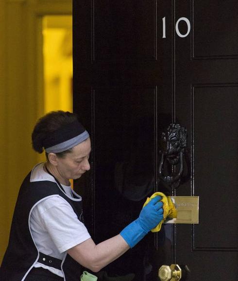 Una empleada limpiando la puerta del número 10 de Downing Street.