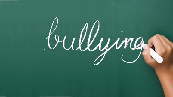 Un niño escribe en una pizarra la palabra 'bullying'. 