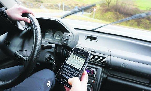 Un joven escribe en su 'smartphone' un mensaje de Whatsapp mientras conduce con la otra mano su coche, una práctica cada vez más habitual y llena de riesgos.