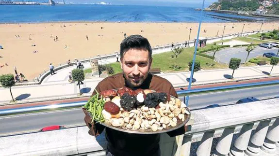Javier Izarra, cocinero del restaurante Tamarises Izarra, sostiene una bandeja con productos de temporada ante la playa de Ereaga. 