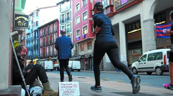 Una persona junto a un cartel en el que pide ayuda en una acera de una calle de Eibar.
