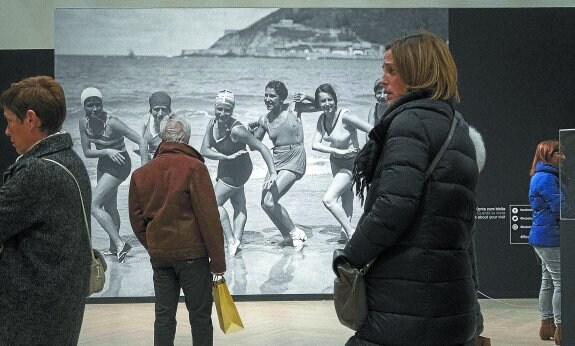 Visitantes observan algunas de las grandes fotos de la exposición, como la que muestra a mujeres bañistas en La Concha en los años 30.