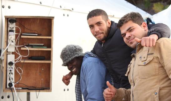 Varios refugiados que viven en el campo de Souda cargan sus dispositivos móviles