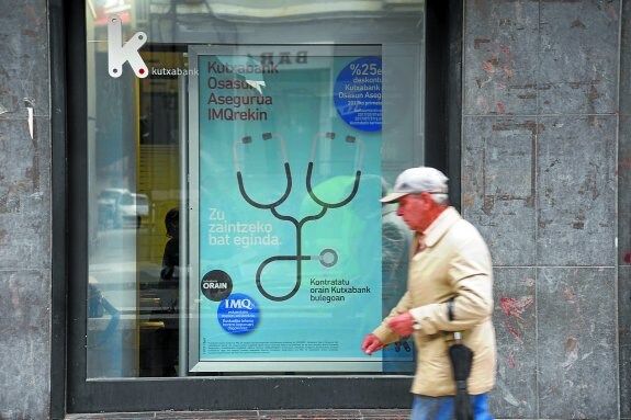 Un hombre pasa ante a una sucursal de Kutxabank en San Sebastián en la que se publicitan seguros.