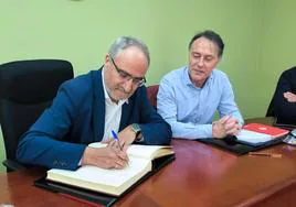 El presidente del Consejo (I) firma en el libro de honor del Ayuntamiento de Cabañas Raras en presencia del alcalde.