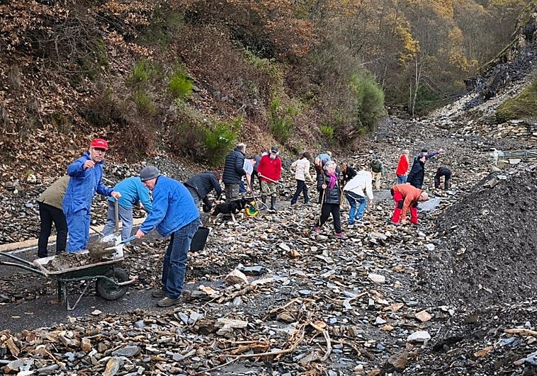 Los vecinos de Peñalba de Santiago retiran con sus propias manos la piedras y el barro del argayo que invade la carretera de acceso al pueblo.