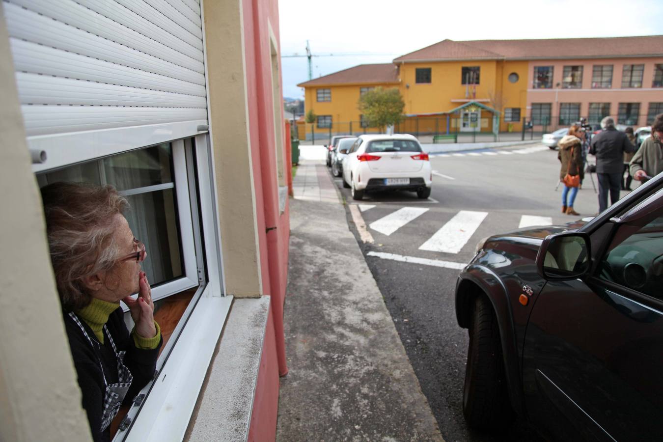 Una vecina, con gesto abatido, observa la calle desde su ventana.