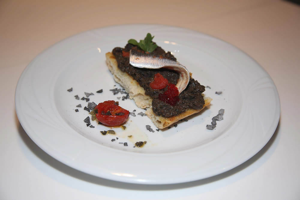 Sardina de roca (El Puente). Sardina de roca marinada sobre tostada de tapenade, con tomatitos aliñados y escamas de sal de carbón.