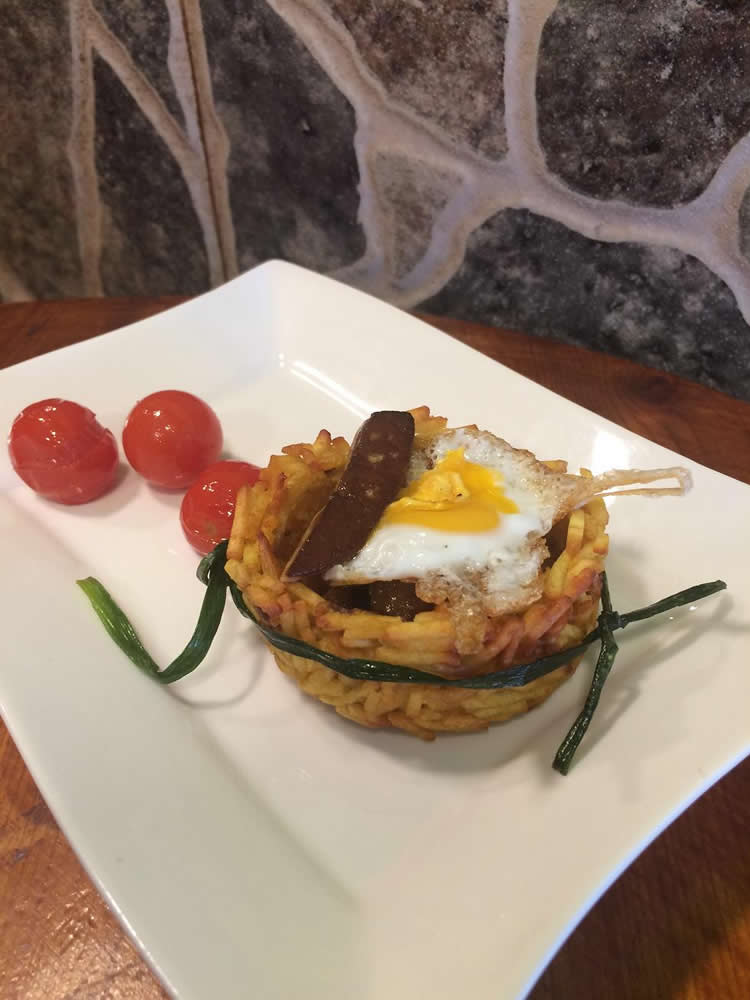 El Neñu (El Colón Sidrería). Nido de patatas paja con carrillera ibérica, frutos secos, foie y corona de huevo de codorniz.