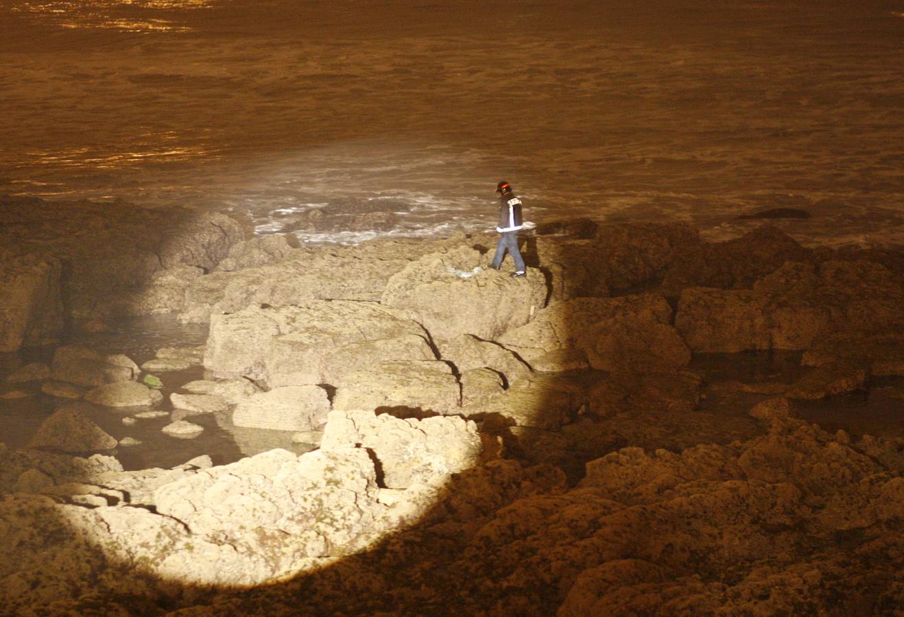 Un bombero camina sobre las rocas del pedreru del Rinconín bajo el rayo de luz de un potente foco durante las tareas de búsqueda del cuerpo de un hombre que un surfero creyó ver en el agua. 07/05/2009