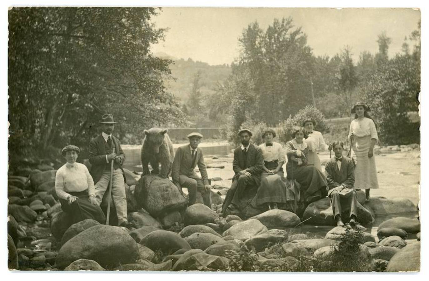 Foto anónima realizada probablemente en la segunda década del siglo pasado, a la orilla del río Piloña a su paso por Infiesto. Aparecen Concha Guisasola y Pepito Argüelles, propietario del oso con amigos y familiares. La foto ha sido cedida para su reproducción digital por Roque Rodríguez-Noriega Guillén.
