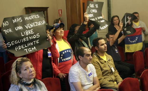 Venezolanos residentes en Oviedo muestran sus pancartas opositoras durante el Pleno.