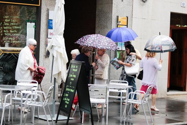 Los turistas se refugian bajo el paraguas en Gijón. 