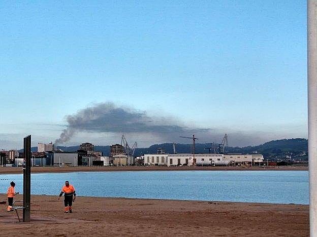 Un operario de Emulsa camina por la playa de Poniente, con una nube de los complejos industriales de la zona oeste al fondo. 