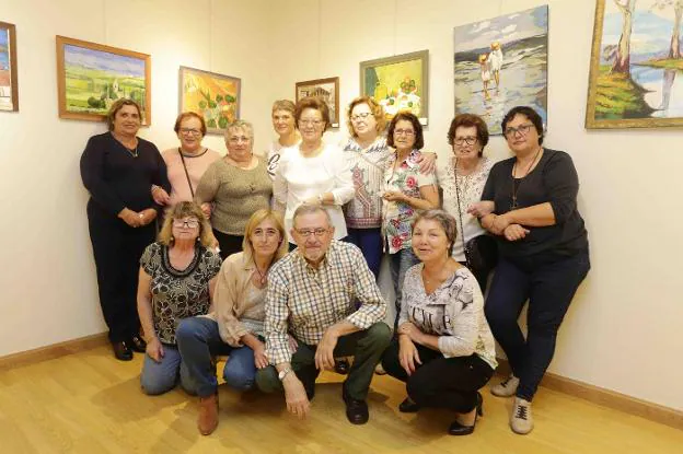 Las integrantes del taller de pintura, con Carlos Jiménez, y parte de los cuadros expuestos. 
