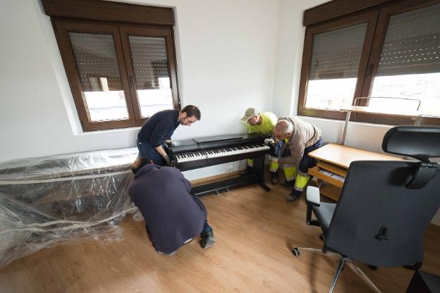 Profesores y operarios municipales instalan un piano. 