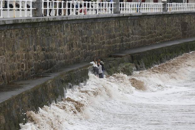 Tres jóvenes se agarran a unas rocas del Muro, en Gijón, para evitar que una ola les arrastre. 