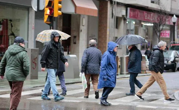 Varias personas pasean bajo la lluvia por Gijón.