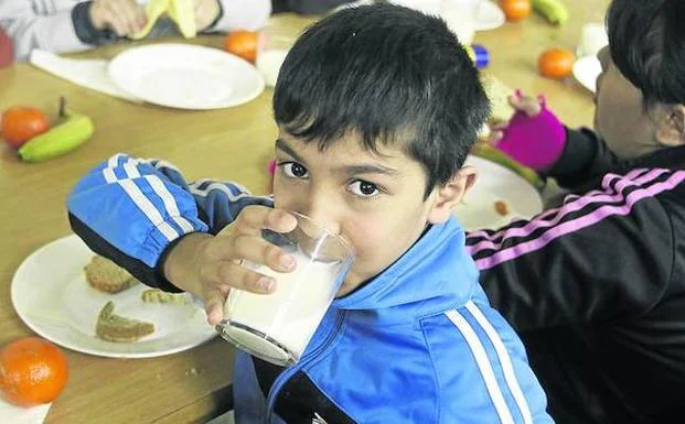 Unos niños toman leche y fruta en un comedor escolar. 