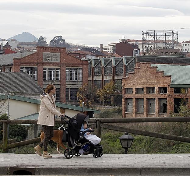 Un mujer paseo a un bebé y un perro delante de La Vega. 