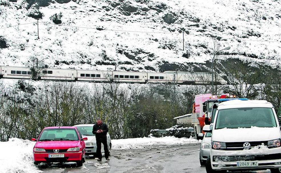 Un tren avanza hacia Pajares pese a la nevada mientras los turismos esperan en un aparcamiento de Campomanes la apertura de las carreteras. 