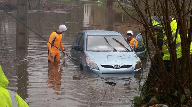 Dos voluntarios de Protección Civil de Piloña sacan un coche de un canal desbordado en Biedes. 