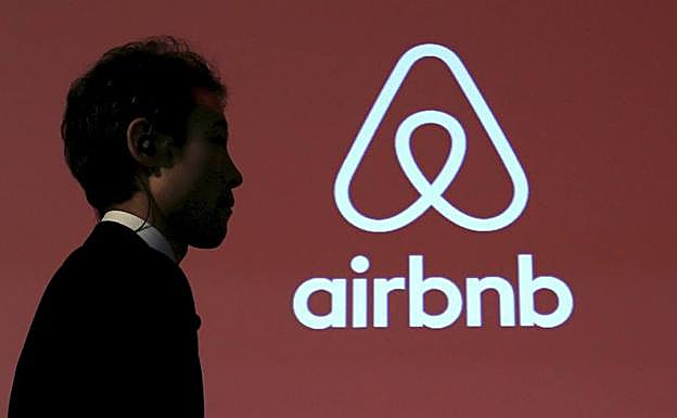Un hombre camina junto a un logosímbolo de Airbnb. 