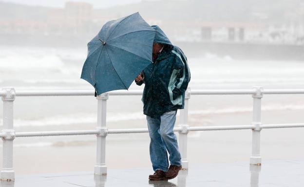 Un hombre camina bajo la lluvia en Gijón.