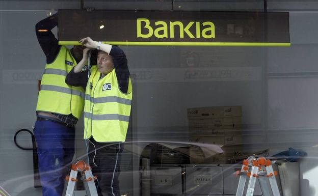 Dos trabajadores colocan un cartel de Bankia en una oficina de Madrid. 
