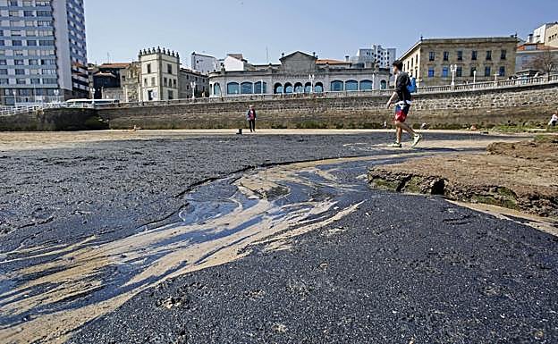 Imagen. Usuarios de la gijonesa playa de SanLorenzo sorteando ayer la mancha de carbón aparecida en el arenal.