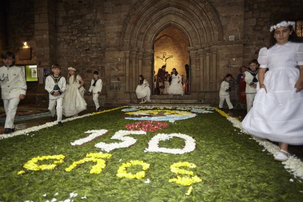 Los niños salen de la iglesia vestidos de Primera Comunión sobre una alfombra de flores. 