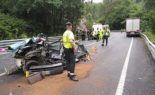 Bomberos y agentes de la Guardia Civil, junto a los restos del vehículo siniestrado el viernes en la N-640. 