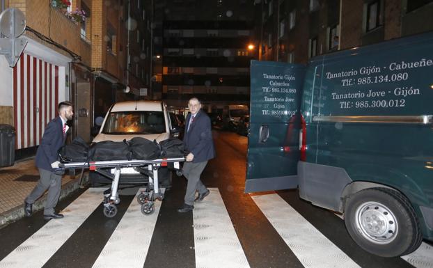 Los empleados de la funeraria trasladan uno de los cadáveres al interior del furgón fúnebre, en la calle Felicidad. 