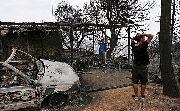 Varios residentes observan los destrozos registrados en una propiedad tras el paso de las llamas en Mati (Grecia).