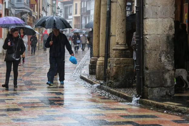 Un grupo de peatones, ataviados con paraguas y abrigos en el inicio de la calle de Rivero. 